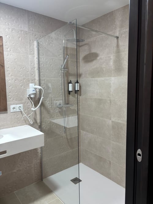 Modern bathroom shower with beige tile walls and glass enclosure at Hotel Mulhacén Trevélez, Granada