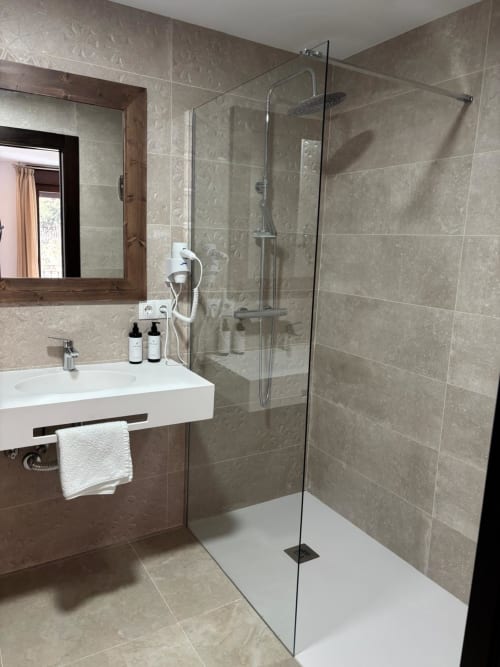 Modern bathroom at Hotel Mulhacén Trevélez with walk-in shower, white sink, mirror, and beige tiled walls.