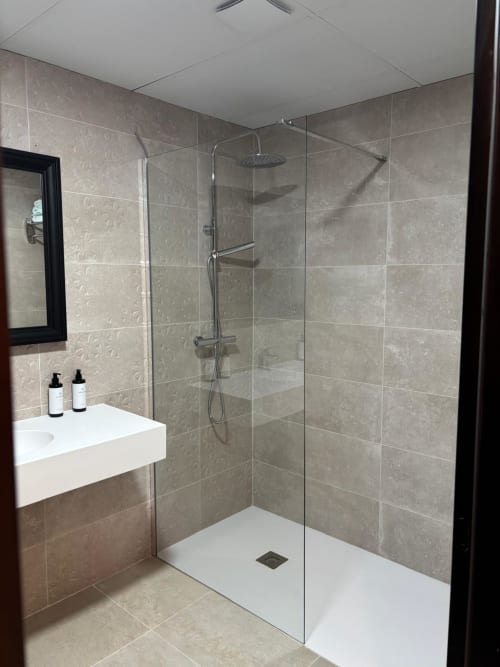 Modern bathroom with walk-in shower at Hotel Mulhacén Trevélez, Granada. Features gray tiled walls, glass enclosure, rainfall