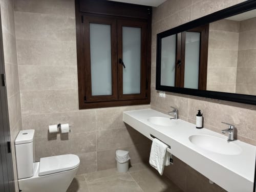 Modern bathroom at Hotel Mulhacén Trevélez with dual sinks, toilet, and dark wood window frames in Trevélez, Granada