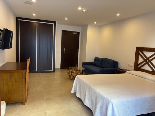 Spacious hotel room at Hotel Mulhacén Trevélez with bed, sofa, wooden desk, and balcony doors in Granada