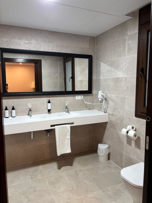 Modern bathroom at Hotel Mulhacén Trevélez with white sink, black-framed mirror, beige tiles, toilet, and amenities