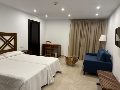 Spacious hotel room at Hotel Mulhacén Trevélez with white bed, blue sofa, desk, and modern amenities in Granada
