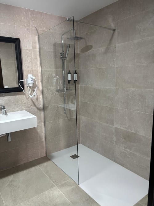 Modern bathroom with walk-in shower, glass enclosure, and stone tile at Hotel Mulhacén Trevélez, Granada