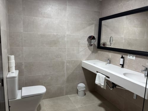 Modern bathroom in Hotel Mulhacén Trevélez with white vanity sink, toilet, tile walls, and large mirror