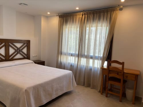 Habitación doble del Hotel Mulhacén Trevélez con vistas a la montaña, cama de madera y cortinas beige