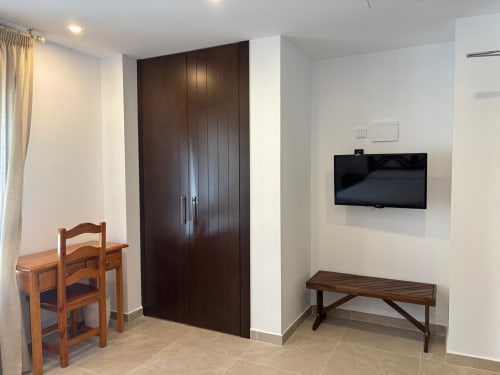 Habitación doble del Hotel Mulhacén Trevélez con armario de madera oscura, TV mural, muebles de madera y vistas a la montaña