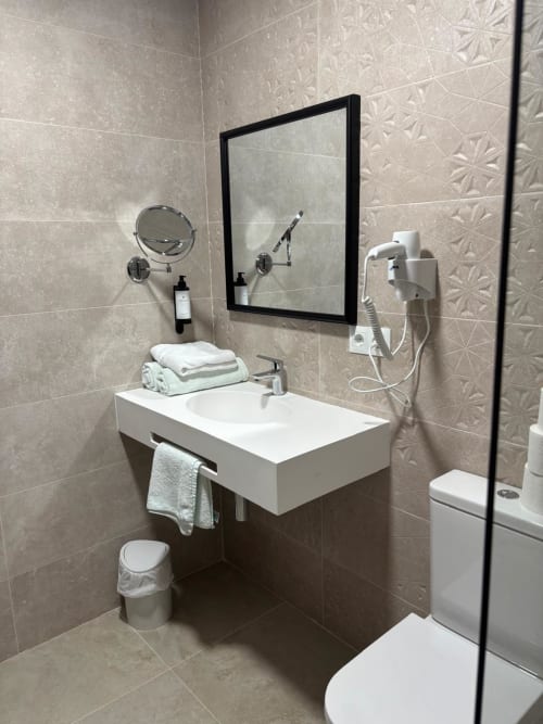 Baño moderno del Hotel Mulhacén Trevélez con lavabo blanco, espejo, artículos de tocador y ducha en Granada