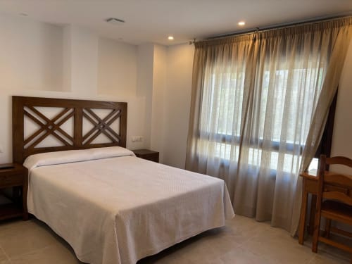 Luminosa habitación doble en Hotel Mulhacén Trevélez con cama de madera, vistas a la montaña desde grandes ventanales, Granada España