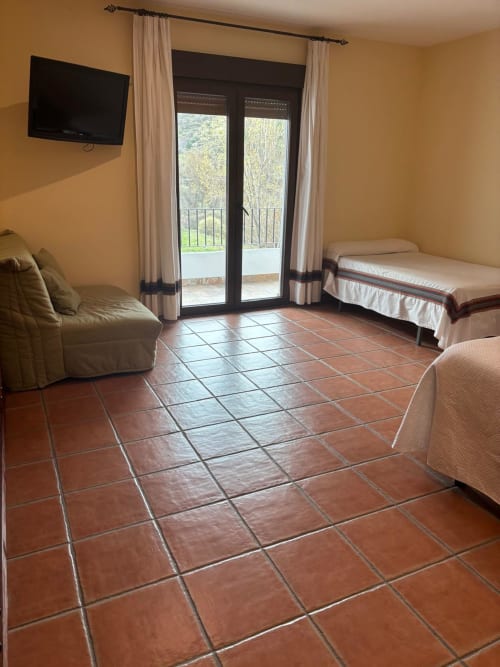 Suite Senior Familiar with terrace at Hotel Mulhacén Trevélez, featuring two beds, sofa, terrace doors with river and