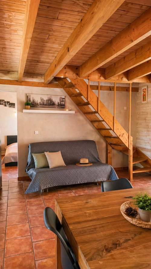 Intérieur de villa en bois avec escalier mezzanine, canapé, coin repas et poutres apparentes au Maquis Plage, Poggio-Mezzana
