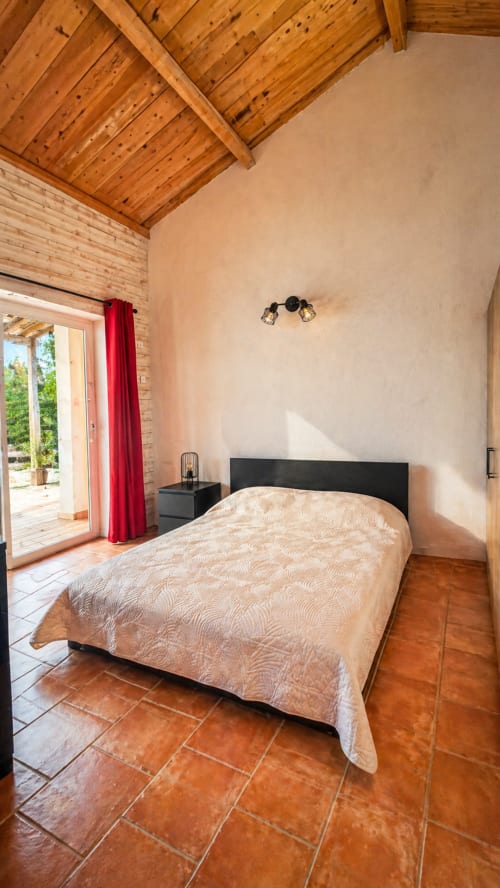 Spacieuse chambre de la villa Le Maquis Plage avec plafond en bois, carrelage en terre cuite et portes-fenêtres ouvrant sur le jardin.