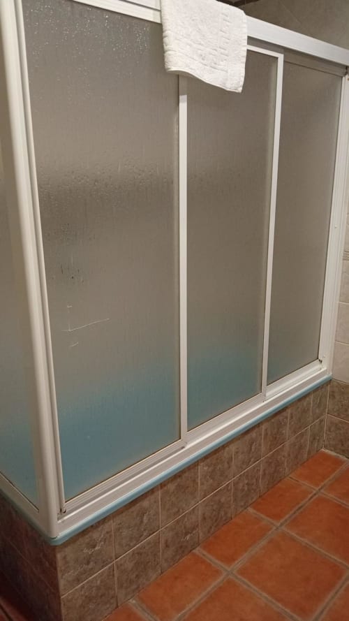 Bathroom shower enclosure with frosted glass doors and white frame at Hotel Mulhacén Trevélez