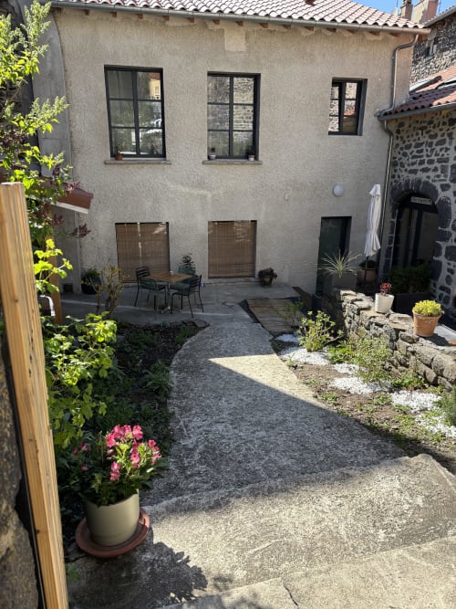 Cour de l'auberge En si bon chemin à Le Monastier sur Gazeille avec coin détente, fleurs en pots et bâtiment en pierre
