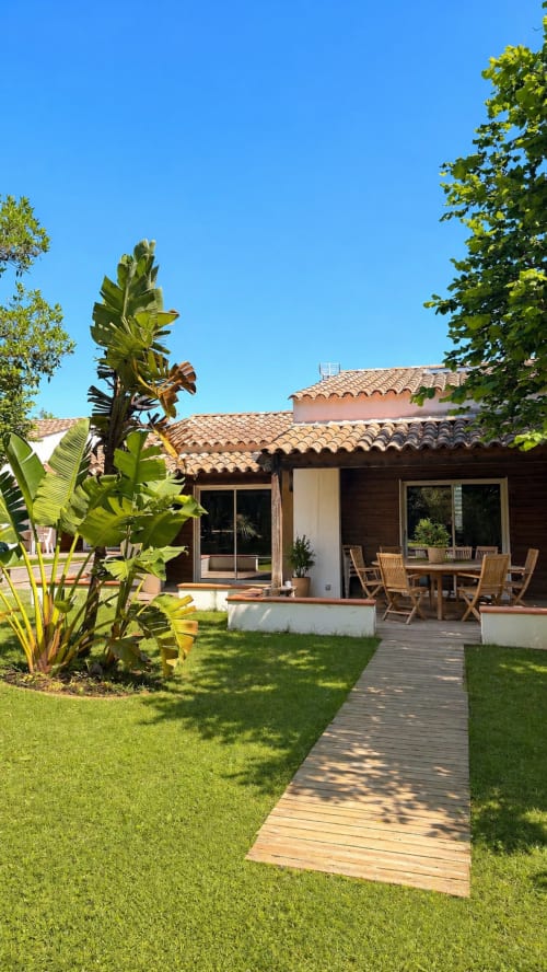 Terrazza dell'hotel Le Maquis Plage con ponte in legno, giardino, piante tropicali e area ristorazione a Poggio-Mezzana