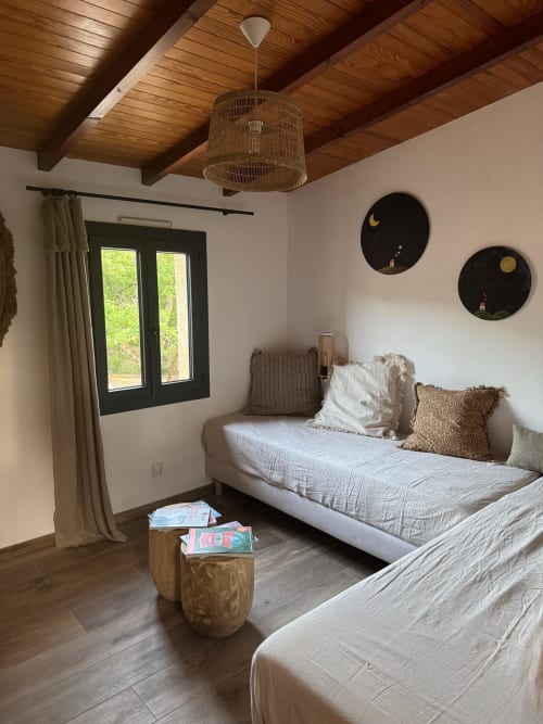 Chambre lumineuse à la Maison Terre de Lune avec poutres en bois, lits jumeaux, luminaire en rotin et vue sur la forêt