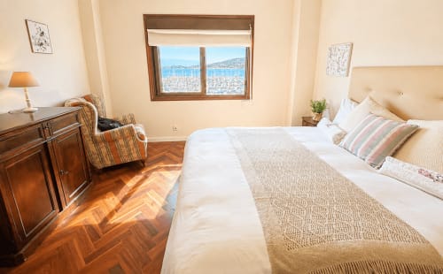 Dormitorio luminoso en apartamento de Baiona con vista al mar, muebles de madera y veleros visibles desde la ventana