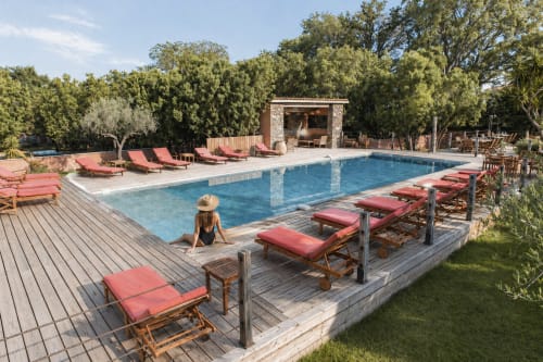 Femme relaxant à la piscine du Maquis Plage avec transats rouges, pavillon en pierre et arbres à Poggio-Mezzana