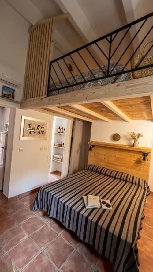 Modern loft bedroom at Le Maquis Plage with mezzanine bed, wood beams, striped bedding, and bathroom access