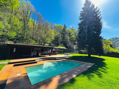 Piscina turquesa amb terrassa de fusta amb vistes a luxuriants jardins i muntanyes boscoses a la villa El Niu de l'Aguila