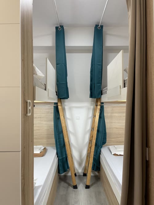 Vista aérea de habitación compartida en Therma Pilgrim Hostel con dos camas individuales separadas por cortinas turquesas y madera