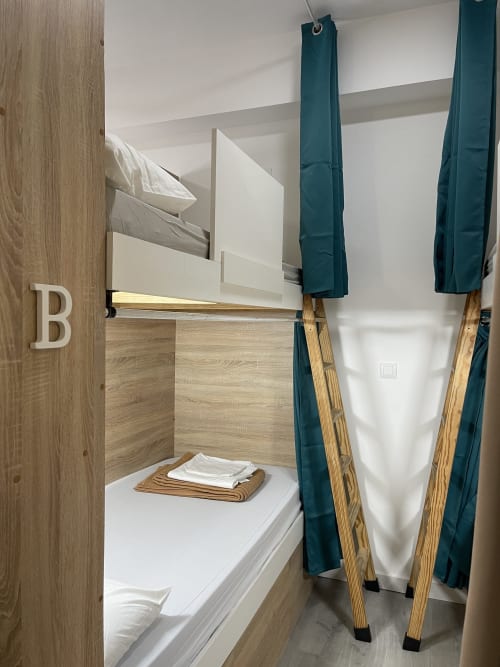Cama litera en cabaña del Hostal Therma Pilgrim en Caldas de Reis con escalera de madera, cortinas verde azulado y toallas dobladas sobre el colchón.