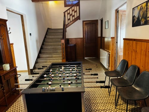 Spaciosa sala de jocs a la villa El Niu de l'Aguila amb futbolí, cadires negres, lambrissat de fusta, escala i rajoles