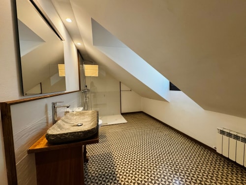 Bany modern a l'assotanat de la villa El Niu de l'Aguila amb pica de pedra, dutxa oberta, sòl de rajoles geomètriques i claraboia