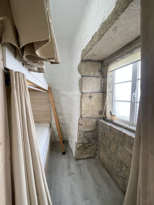 Habitación compartida estrecha en el Therma Pilgrim Hostel con paredes de piedra, ropa blanca, literas y ventana en Caldas de Reis