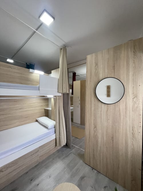 Moderna habitación compartida en Therma Pilgrim Hostel con literas, interiores de madera, espejo circular e iluminación LED