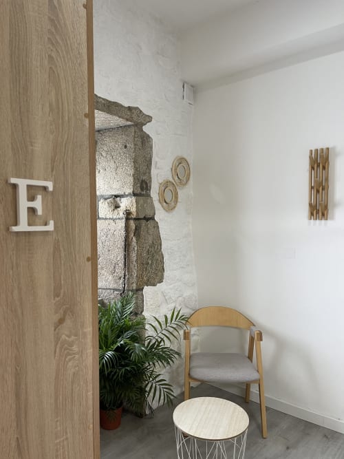 Acogedora habitación en el albergue Therma Pilgrim con puerta de madera, paredes blancas, detalle en piedra, planta verde, silla de madera y decoración moderna