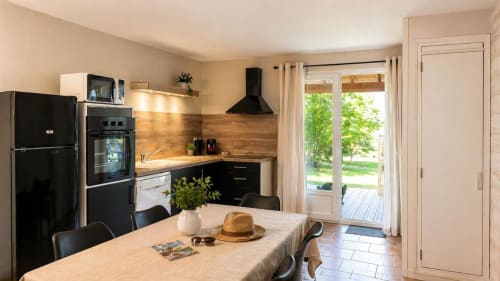Cuisine et salle à manger modernes de la villa Le Maquis Plage avec électroménagers noirs, plan de travail en bois et vue sur le jardin