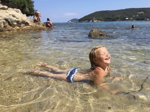 Young girl swimming in crystal-clear turquoise water at Marina di Campo beach near Casa Pineta, Italy