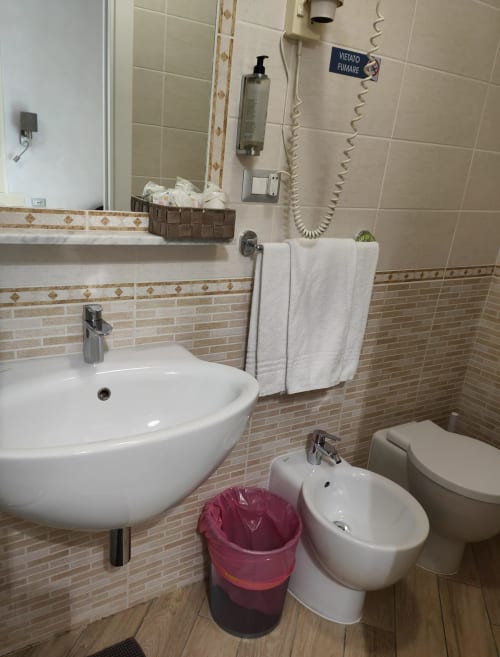 Bagno moderno dell'Hotel Principe Amedeo con lavabo rotondo bianco, bidet, wc e pareti piastrellate con bordi decorativi
