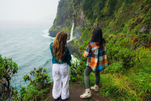 Dos mujeres observando los acantilados costeros y una cascada cerca de Les Terrasses Les Suites en Calheta, Portugal
