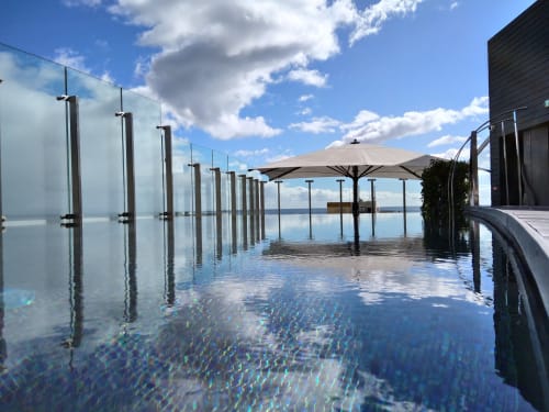 Piscina infinita con barandillas de cristal y sombrilla beige en el hotel Les Terrasses Les Suites, Calheta Portugal