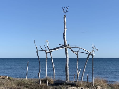 Installazione artistica di legni trascinati sulla spiaggia vicino a Casale Artemisia, Capalbio con mare calmo e cielo sereno