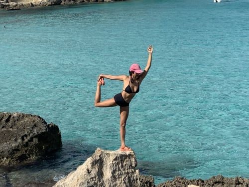 Donna in posizione yoga sulle rocce costiere di Casale Artemisia, Capalbio, con le acque turchesi del Mediterraneo