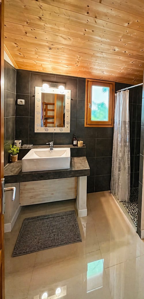 Modern bathroom at Le Maquis Plage with wooden ceiling, black tiles, white vessel sink, and walk-in shower in Poggio-Mezzana