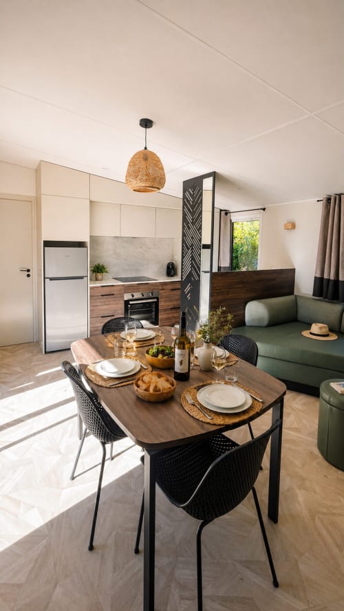 Modern open-plan studio at Le Maquis Plage with dining table, equipped kitchen, and green sofa overlooking Poggio-Mezzana