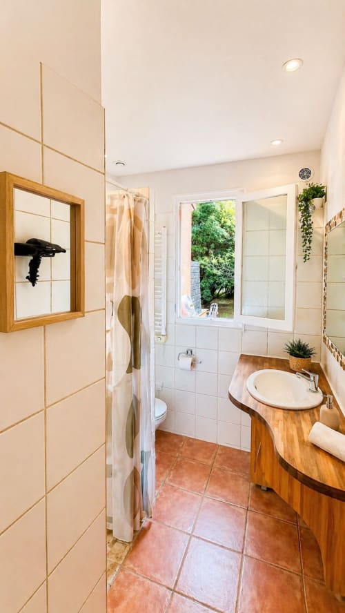 Bagno moderno dell'hotel Le Maquis Plage a Poggio-Mezzana con vanità in legno, piastrelle bianche e vista sul giardino