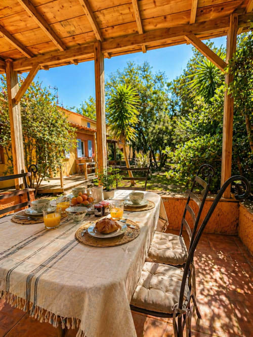 Terrazza colazioni dell'hotel Le Maquis Plage con pergolato in legno, tavolo apparecchiato e vista sul rigoglioso giardino corso