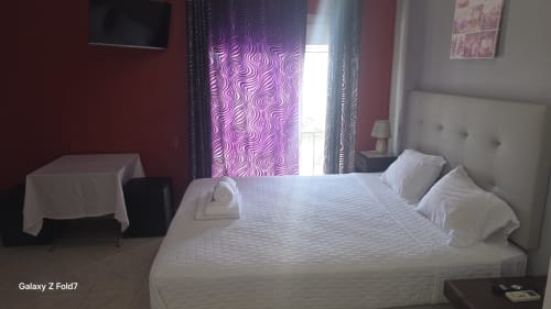 Quarto luminoso na AL Hospedaria Pôr do Sol, Olhão com cama branca, cortinas roxas estampadas, paredes vermelhas e vista da cidade
