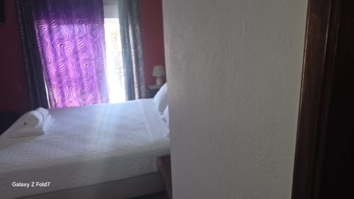Quarto do AL Hospedaria Pôr do Sol em Olhão com cama branca, cortinas com padrão roxo e vista para a cidade