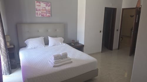 Quarto moderno da AL Hospedaria Pôr do Sol em Olhão com cama estofada cinzenta, roupa de cama branca, TV de ecrã plano e vista para a cidade.