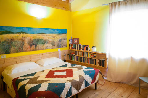 Dormitorio amarillo brillante en Casale Artemisia B&B en Capalbio con cama de madera, colcha patchwork colorida y estantería