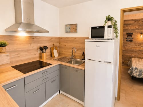 Kitchenette moderne de la villa Le Maquis Plage avec comptoirs en bois, évier inox, électroménagers blancs et armoires grises