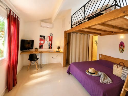Mini-villa avec mezzanine à Le Maquis Plage : lit violet, plateforme en bois, bureau et rideaux rouges