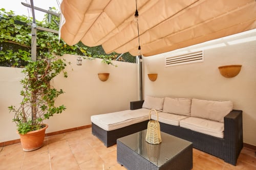 Acogedora zona de estar en el patio de Experiencias Encant con muebles tapizados en beige, pérgola y plantas en macetas