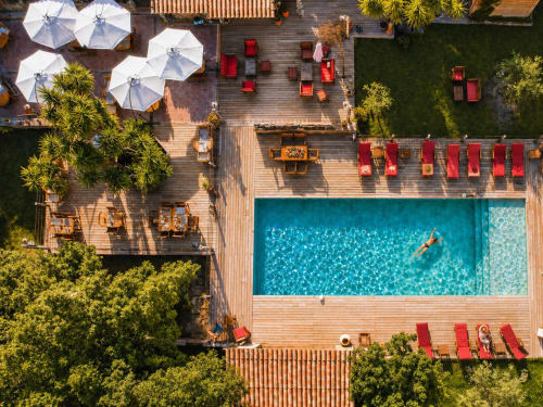 Vue aérienne de l'hôtel Le Maquis Plage à Poggio-Mezzana avec piscine turquoise, transats rouges et parasols blancs
